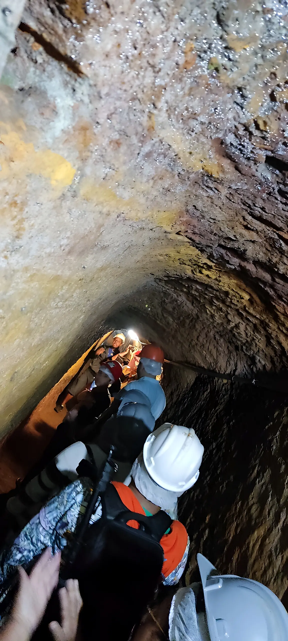 Visitantes de capacete passando por um trecho estreito do túnel